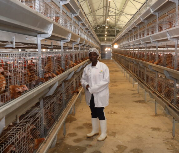 A happy farmer stands proudly in her flourishing poultry farm, which has thrived thanks to Plum's services.